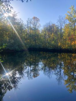 gorgeous sunbeams, autumn woods and  and blue sky reflected in lake. Beautiful calming symmetry with copy space.