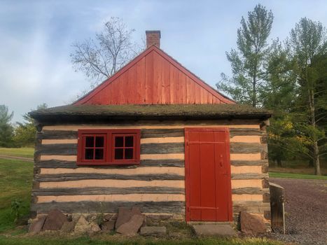 Beautiful historic log construction with stone foundation and stepping stone threshold in nature setting. Full frame image in natural light, with 4-pane windows and long hinges.