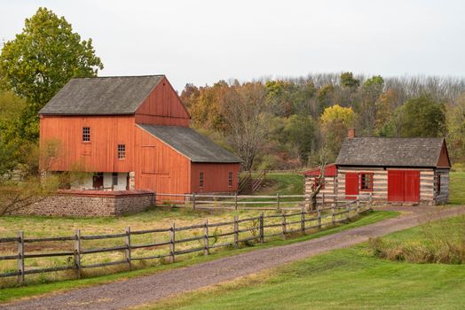 Historic colonial American farm scene, dirt road, log cabin and red barn on the historic Daniel Boone Homestead in Pennsylvania.