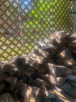 Beautiful dappled light spills acrodd the cut wood. cord wood is stacked and ready for winter in comforting full frame image with copy space.