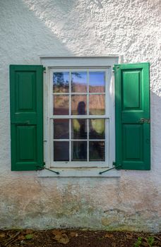 Beautiful old glass shows wavy reflection framed by green wooden shutters on a white colonial American house,