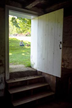 Door to the historic spring house at Hopewell Furnace National Historic Site is open, a young woman sits in the summer sunshine reading a book. Beautiful full-frame image with copy space.