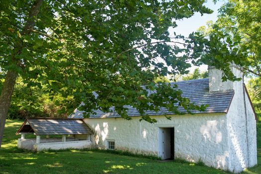 Beautiful full frame image of a colonial whitewashed stone springhouse surrounded by natural green grass and lush summer foliage.