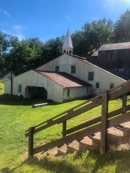 Steps lead down to the beautiful old historic Pennsylvania iron furnace. A cannon lays in the grass by the doorway in idyllic colonial American scene. Bright summer sunshine with copy space.