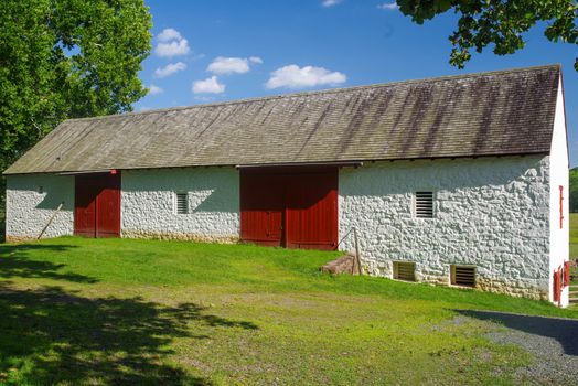 Colonial barn at the Hopewell Furnace National Historic Site in Pennsylvania. Massive, elegant whitewashed stone with red doors and ventilation windows. Notice the rat tail hinges on the doors. Full frame in natural light with copy space.