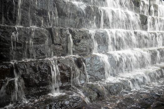 Full frame long exposure image of a tiered waterfall, close up image shows movement and sction of water and rough heft of stone.
