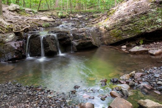 Full frame image of forest waterfall cascading over an ancient rock formation. Water is smooth and reflects forest colors in long exposure shot with copy space.