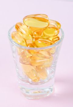 Fish oil capsules in glass on pink background.