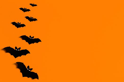 orange background with a flock of black paper bats for Halloween, black paper bat silhouettes on an orange background, Halloween concept, copyspace, flatlay, top view, overhead.