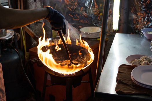 Street food in Bangkok Bangkok Thailand - Oct 24, 2020 :- Chef cooking with fire with frying pan on gas hob at yoawarat Bangkok Thailand.