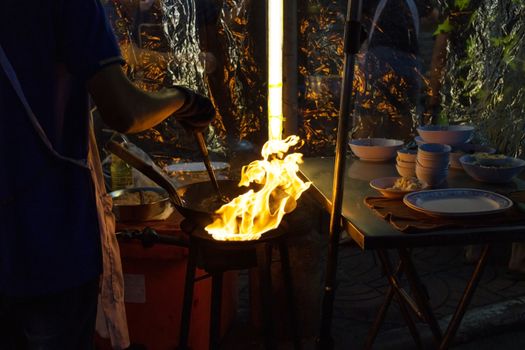 Street food in Bangkok Bangkok Thailand - Oct 24, 2020 :- Chef cooking with fire with frying pan on gas hob at yoawarat Bangkok Thailand.