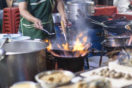 Street food in Bangkok Bangkok Thailand - Oct 24, 2020 :- Chef cooking with fire with frying pan on gas hob at yoawarat Bangkok Thailand.