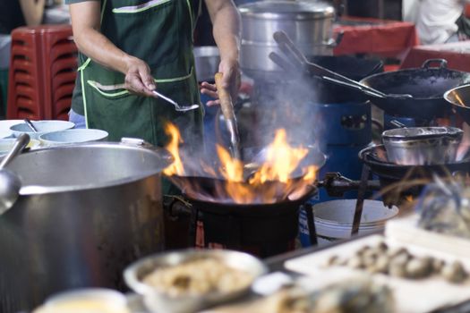 Street food in Bangkok Bangkok Thailand - Oct 24, 2020 :- Chef cooking with fire with frying pan on gas hob at yoawarat Bangkok Thailand.