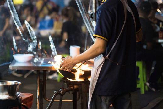 Street food in Bangkok Bangkok Thailand - Oct 24, 2020 :- Chef cooking with fire with frying pan on gas hob at yoawarat Bangkok Thailand.