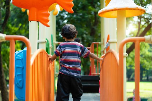 An Asian boy is climbing on a playground equipment in a school.