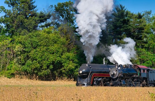 Close up of an 2 Antique Steam Freight Train Puffing Smoke and Steam While going Thru Amish Countryside