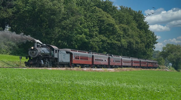 Antique Steam Passenger Train Puffing Lots of Black Smoke along Amish Countryside with Green Fields