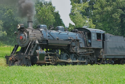 Close Up of an Antique Steam Passenger Train Puffing along Amish Countryside with Green Fields