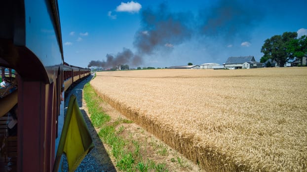 Steam Passenger Train Traveling Along Wheat Field on a Sunny Day