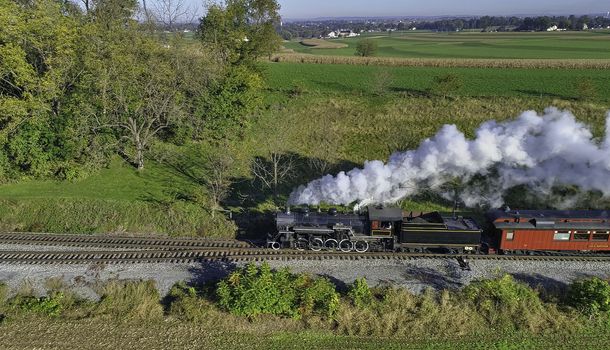 Aerial View of Steam Passenger Train Puffing Smoke Traveling in Amish Countryside in an Early Morning