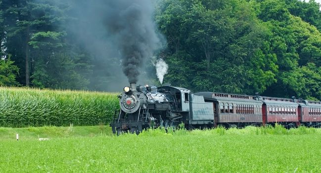 Antique Steam Passenger Train Puffing along Amish Countryside with Green Fields