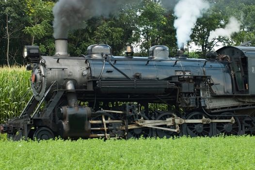 Close Up of an Antique Steam Passenger Train Puffing along Amish Countryside with Green Fields