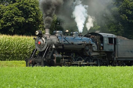 Close Up of an Antique Steam Passenger Train Puffing along Amish Countryside with Green Fields