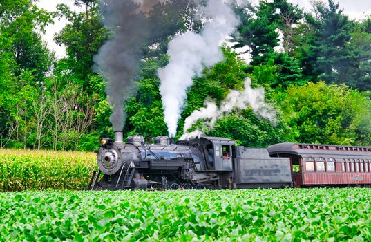 Close Up of an Antique Steam Passenger Train Puffing along Amish Countryside with Green Fields