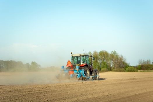 Tractor ploughing the field, dust from dry soil, spring agricultural work