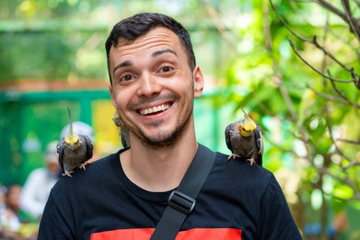 The guy in the bird park communicates with parrots. Tame parrots beg for food from tourists.