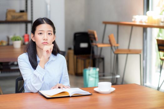 Beautiful of portrait business asian young woman thinking idea and writing on notebook on table, girl work at coffee shop, freelance business concept.