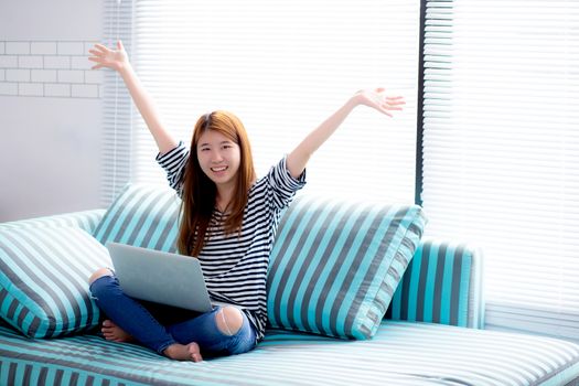 Beautiful happiness portrait of young asian woman using laptop work with success on sofa in the home, girl and notebook internet online with glad, communication concept.