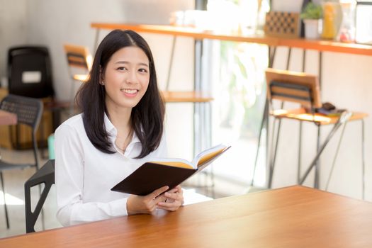 Beautiful of portrait business asian young woman reading on notebook with success on table, girl looking note excited at coffee shop, freelance and education concept.