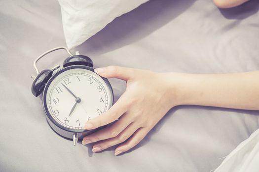 closeup asian young woman turn off alarm clock in good morning, wake up for sleep with  girl holding alarm clock, time and lifestyle concept.