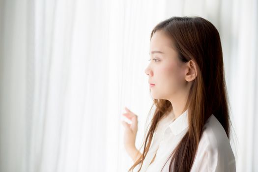 Portrait of beautiful young asian woman standing the window and smile while wake up with sunrise at morning, lifestyle and relax concept.