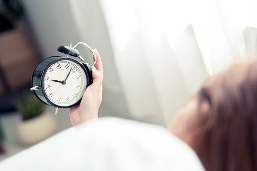 Beautiful asian young woman turn off alarm clock in morning, wake up for sleep with alarm clock, relax and lifestyle concept.