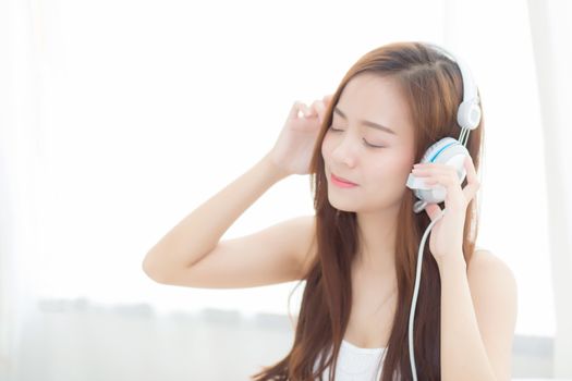 Beautiful asian young woman enjoy listen music with headphone while sitting in bedroom, relax girl with earphone internet online, leisure and technology concept.