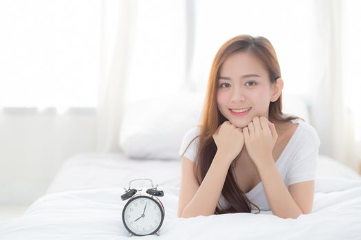 Beautiful of portrait young asian woman wake up in morning and alarm clock, girl standing hurry wake late with appointment with curtain background on bedroom, lifestyle concept.