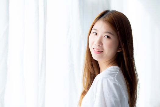 Portrait of beautiful young asian woman standing the window and smile while wake up with sunrise at morning, lifestyle and relax concept.