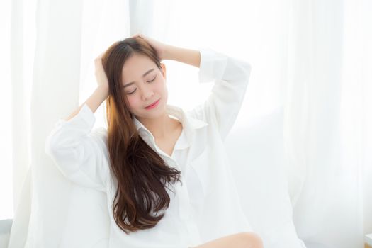 Portrait of beautiful young asian woman standing the window and smile while wake up with sunrise at morning, lifestyle and relax concept.