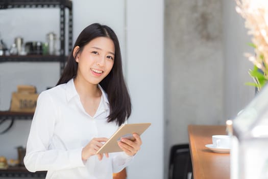 Beautiful portrait young asian woman using tablet computer in the coffee shop, businesswoman sitting looking tablet is work at cafe, communication concept.