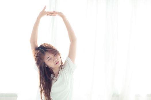 Beautiful young asian woman stretch and relax in bed after wake up morning at bedroom, back view, new day and resting for wellness, lifestyle concept.