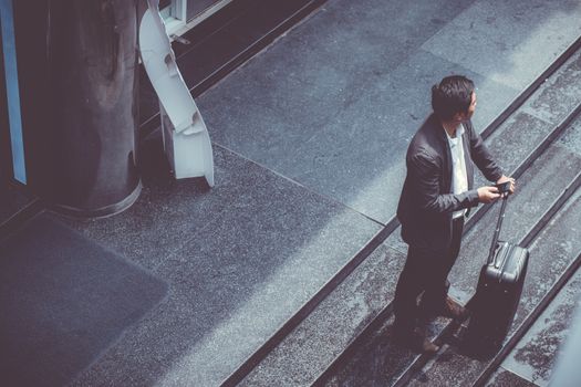 Asian elegant businessman wear suit talking mobile phone while walking holding suitcase outdoor on street, young man contact with customer appointment, communication business concept.