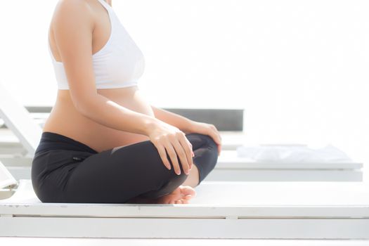 Beautiful pregnant asian young woman relax in the park, closeup girl with belly sitting with crossed leg on grass and yoga exercise for wellness, copy space.