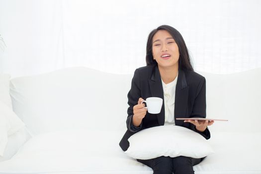 Beautiful of portrait young asian businesswoman sitting on sofa at home looking tablet computer and drinking coffee, woman ralex with internet, communication and business concept.