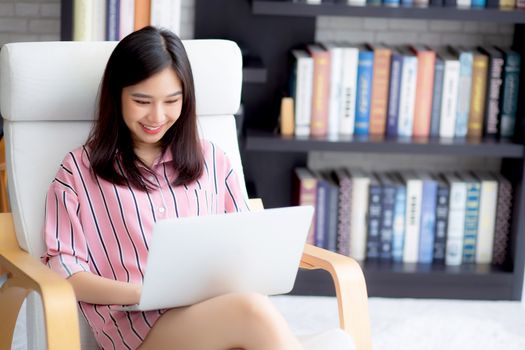 Beautiful of portrait asian young woman working online laptop sitting on chair at living room, girl using notebook computer with connect to internet for distance job, business and success concept.