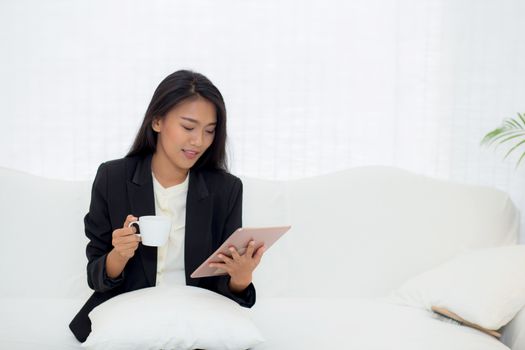 Beautiful of portrait young asian businesswoman sitting on sofa at home looking tablet computer and drinking coffee, woman ralex with internet, communication and business concept.