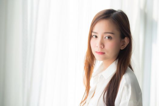 Portrait of beautiful young asian woman standing the window and smile while wake up with sunrise at morning, lifestyle and relax concept.