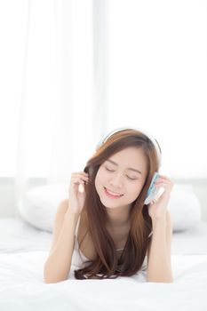 Beautiful asian young woman enjoy listen music with headphone while lying in bedroom, relax girl with earphone internet online, leisure and technology concept.