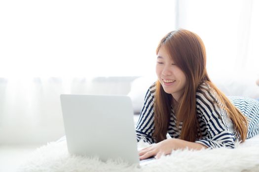 Beautiful of portrait asian young woman lying on bed using laptop at bedroom for leisure and relax, freelance with girl working notebook, communication concept.